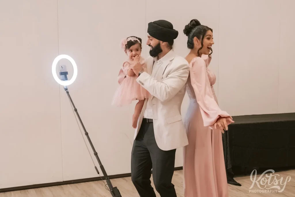 A couple pose in a 360 photo booth with their child.