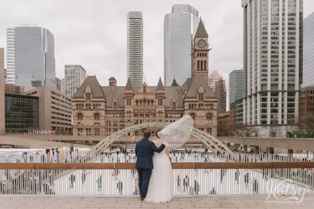 A bride and groom look out into then Nathan Philips Square skating rink after their city hall wedding in Toronto