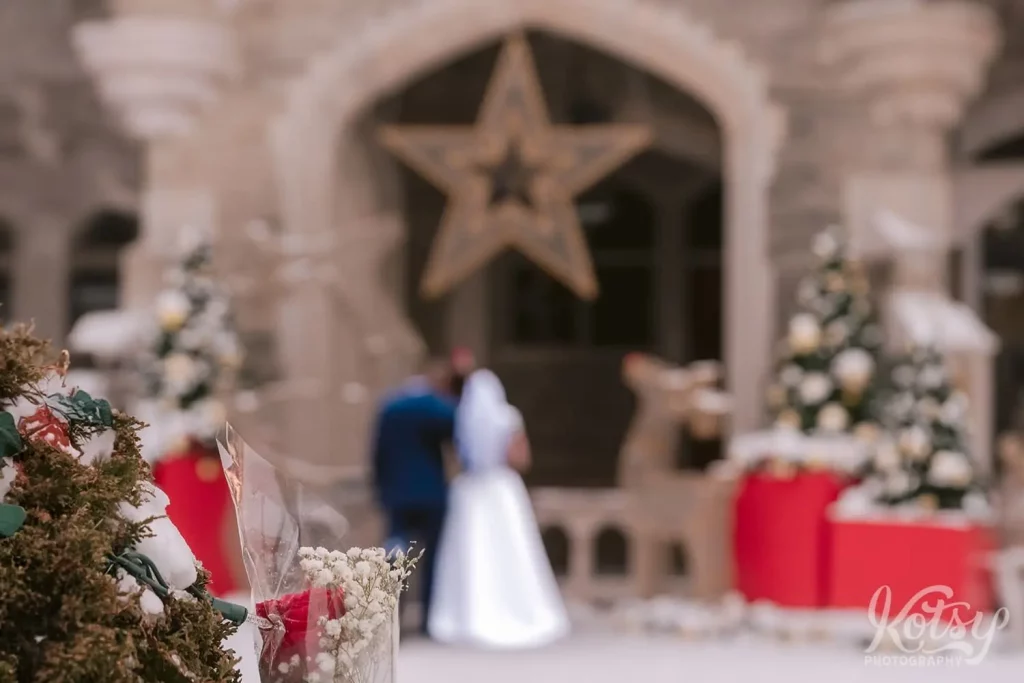 A bride and groom can be seen out of focus past a Christmas tree during their holiday wedding at Casa Loma