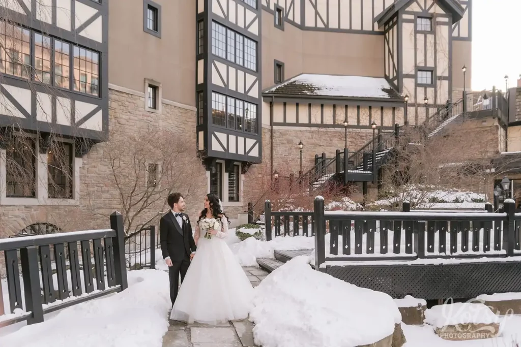 A bride and groom walk through a snow covered courtyard during their winter wedding at Old Mill in Toronto