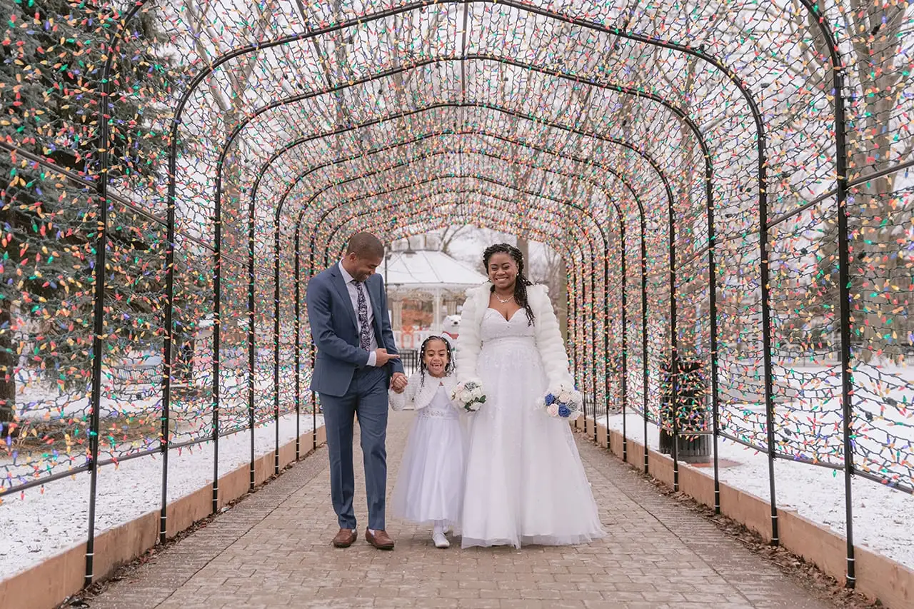 A recently married couple walk through a multi-coloured lit archway after their winter wedding