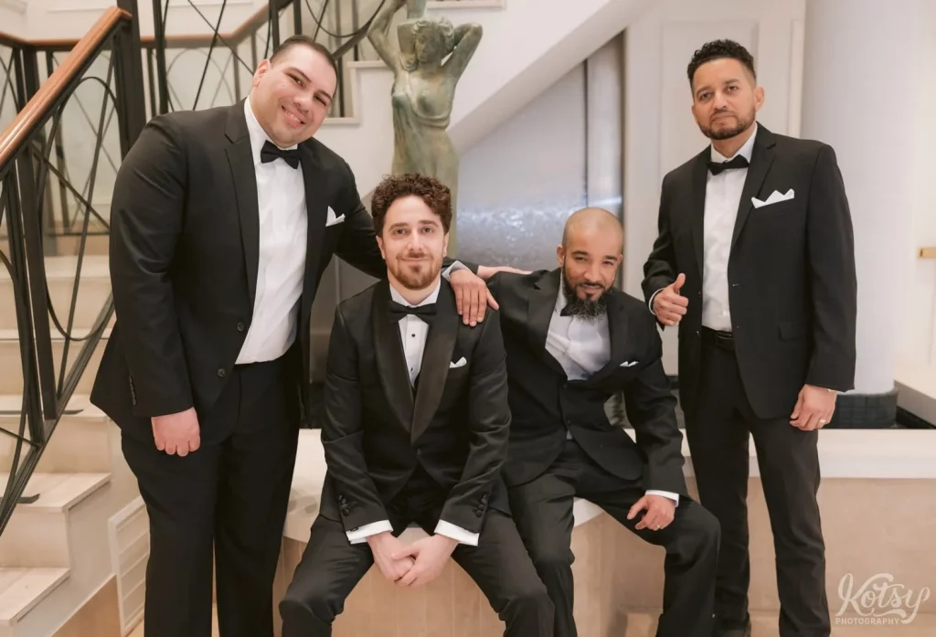 A groom hangs out with his groomsmen by a set of stairs in his condo's lobby in Toronto, Canada