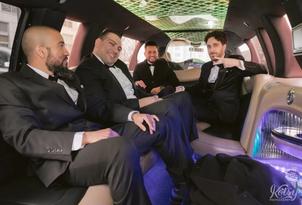 A groom gives the peace sign while sitting in his limo with his groomsmen