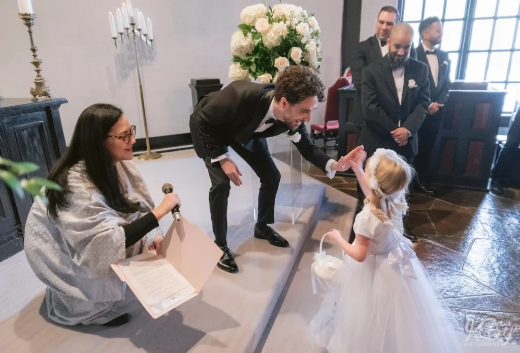 The flower girl gives the groom a high five after making her way down the aisle at a wedding ceremony at Old Mill in Toronto