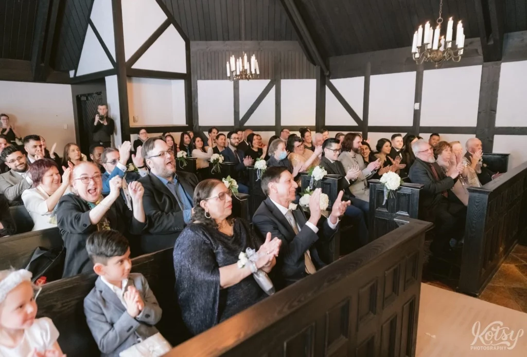 A packed chapel at Old Mill in Toronto cheer loudly for the couple they came to see get married