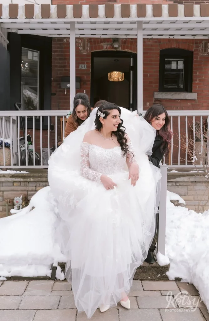A bride in a white wedding gown walks down the steps outside her parents house on the way to her limo on her wedding day