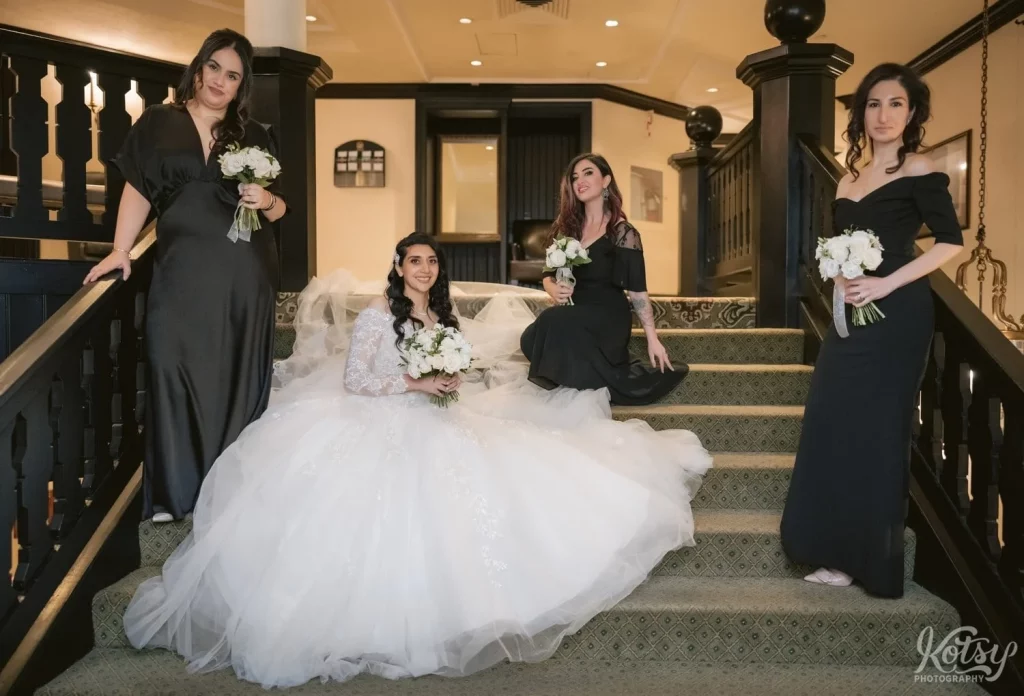 A bride and her bridesmaids smile for the camera on a set of stairs at Old Mill in Toronto