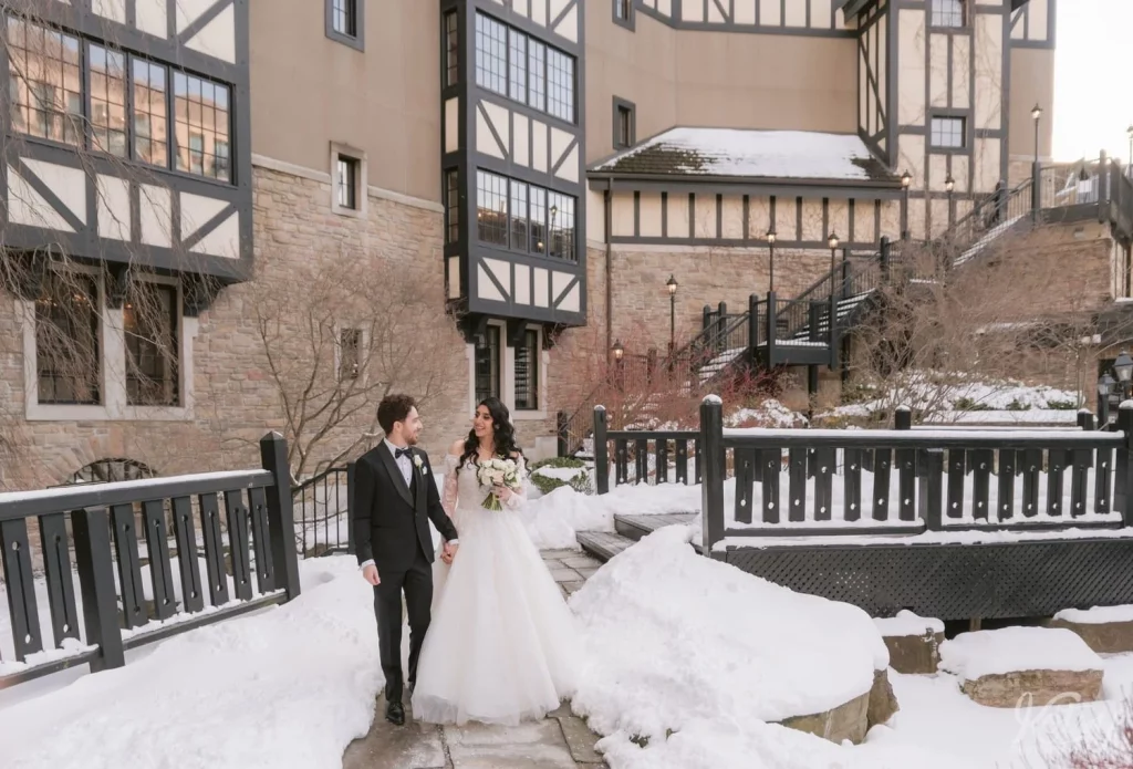 A bride and groom go for a walk in a snow covered courtyard at Old Mill in Toronto
