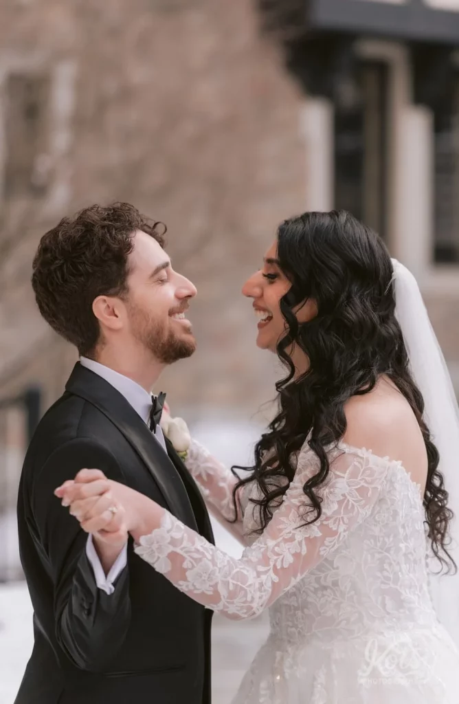 A bride and groom smile as they play with each other's hands in the Old Mill courtyard in Toronto