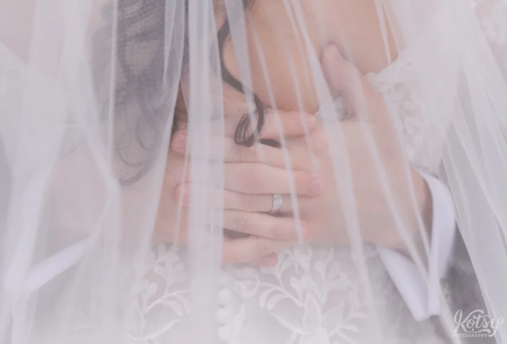 A close up shot of a grooms hands under his bride's veil
