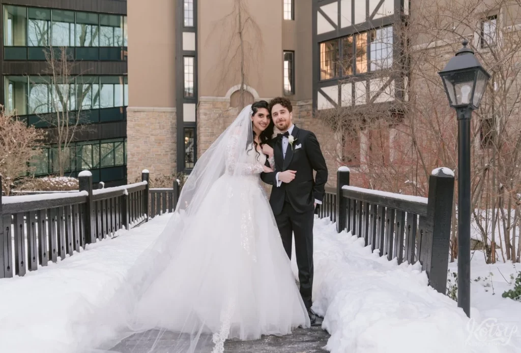 A bride and groom smile for the camera on a snow covered courtyard at Old Mill in Toronto