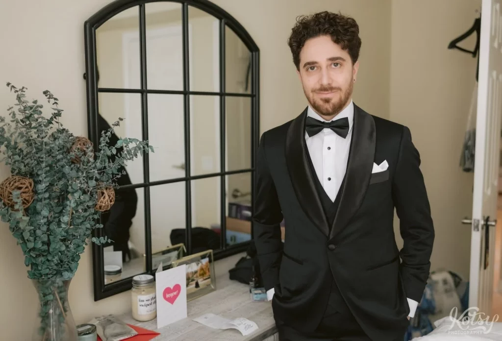 A groom in a black tuxedo smiles for the camera before his wedding at Old Mill in Toronto