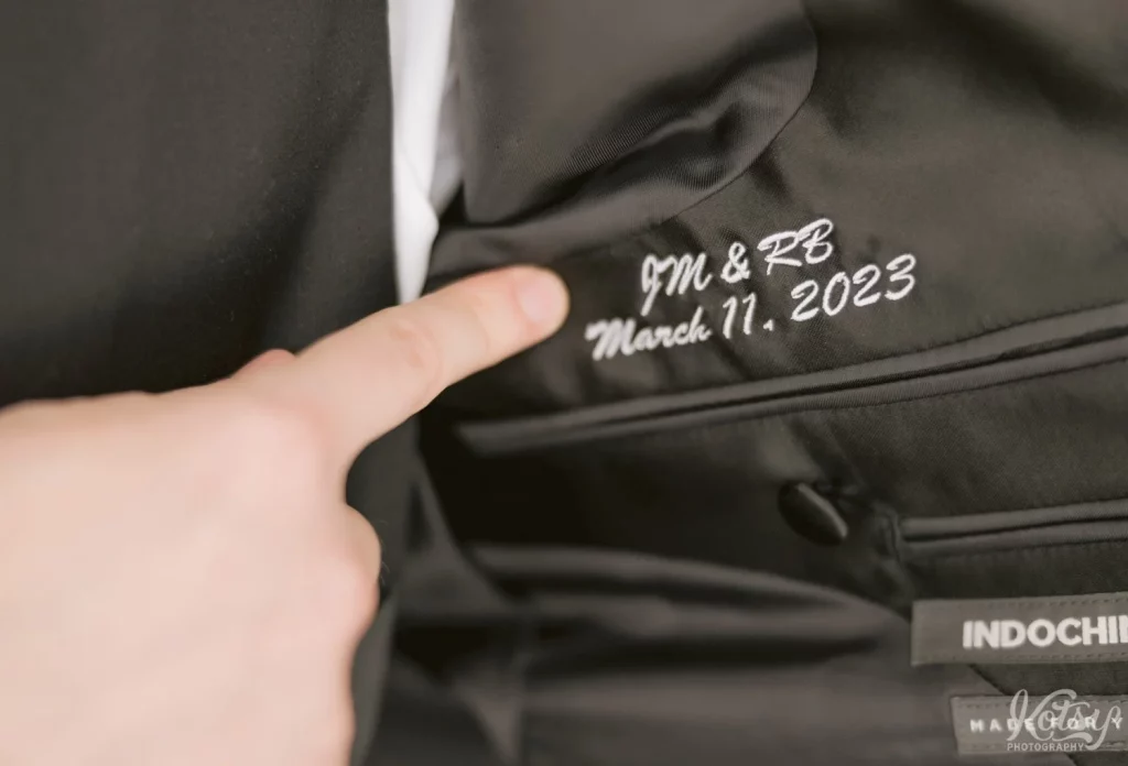 A groom's finger points to an inscription in his tuxedo jacket.