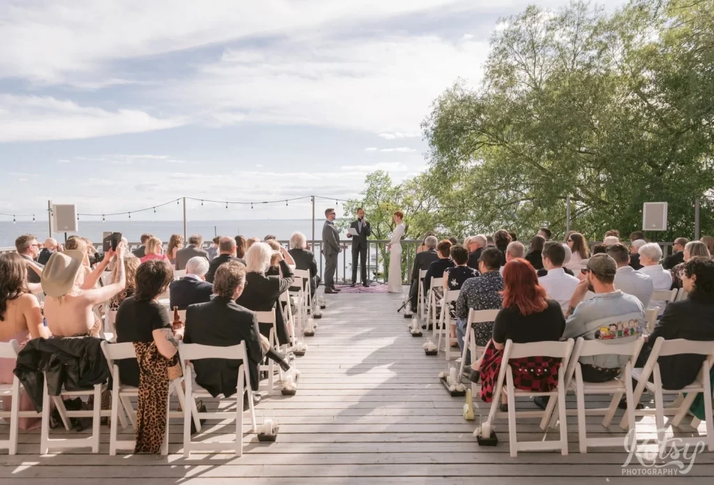 A wide shot of a bride, groom, officiant and large crowd on a lakeside patio at Royal Canadian Legion 344 in Toronto