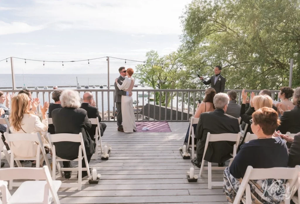 A bride and groom enjoy their first kiss in front of all their guests during their lakeside wedding ceremony