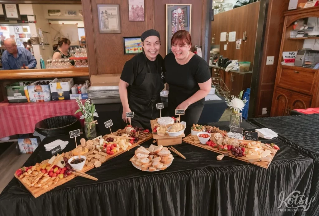Two women from Chau Toronto pose for a picture in front of their food spread at a Royal Canadian Legion wedding in Torono