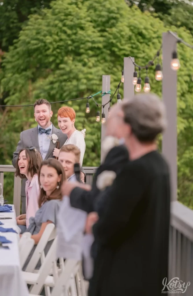 A bride and groom enjoy a laugh during her father's speech at their outdoor wedding in Toronto