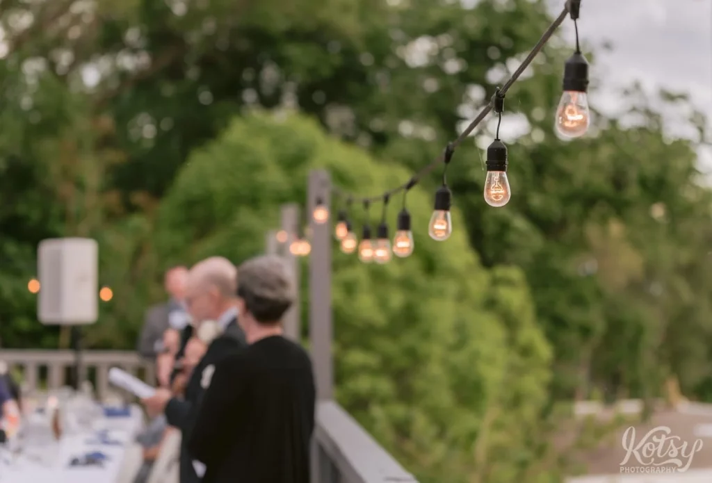 Only a string light is in focus as the bride's father makes a speech at an lakeside wedding in Toronto