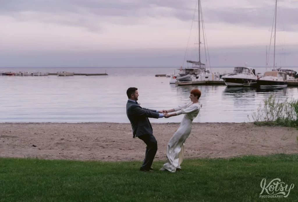 A bride and groom hold each other's hands while spinning in a circle on a beach in Toronto, Canada
