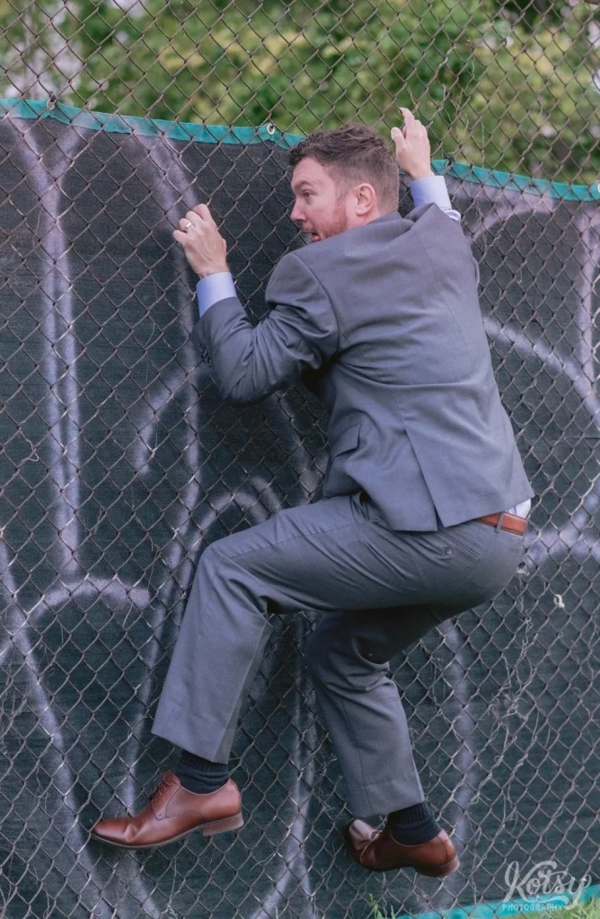 A groom clings to a chain link fence
