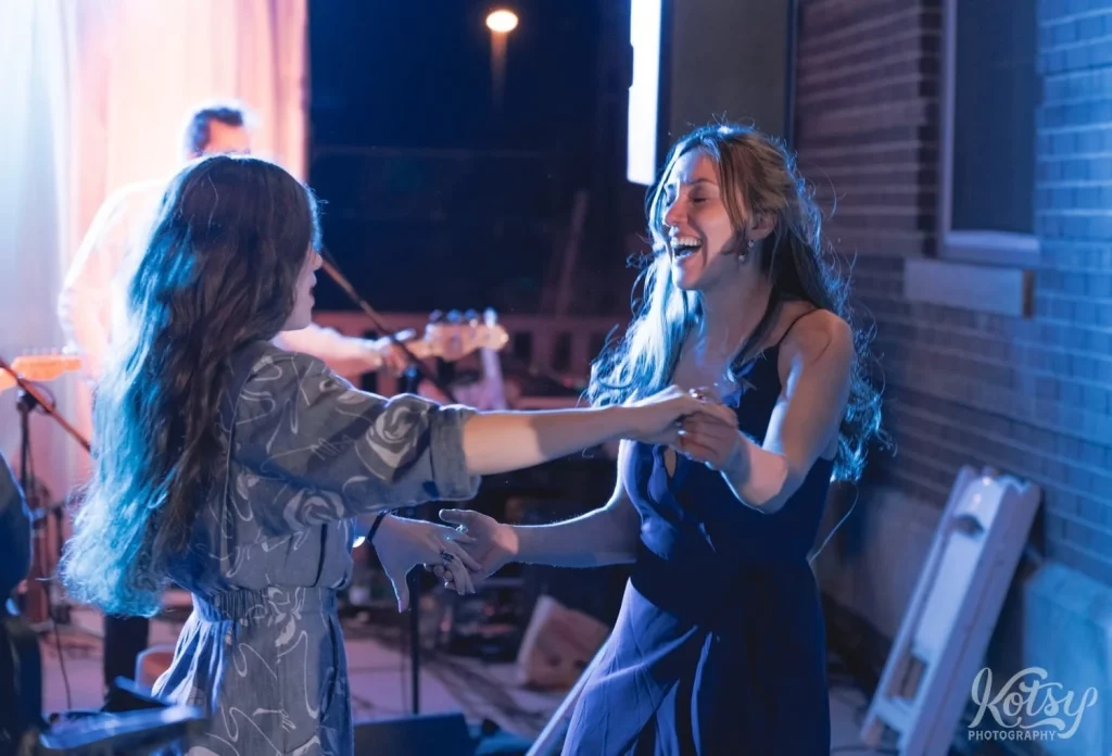 Two women dance hand-in-hand at an outdoor wedding reception in Toronto