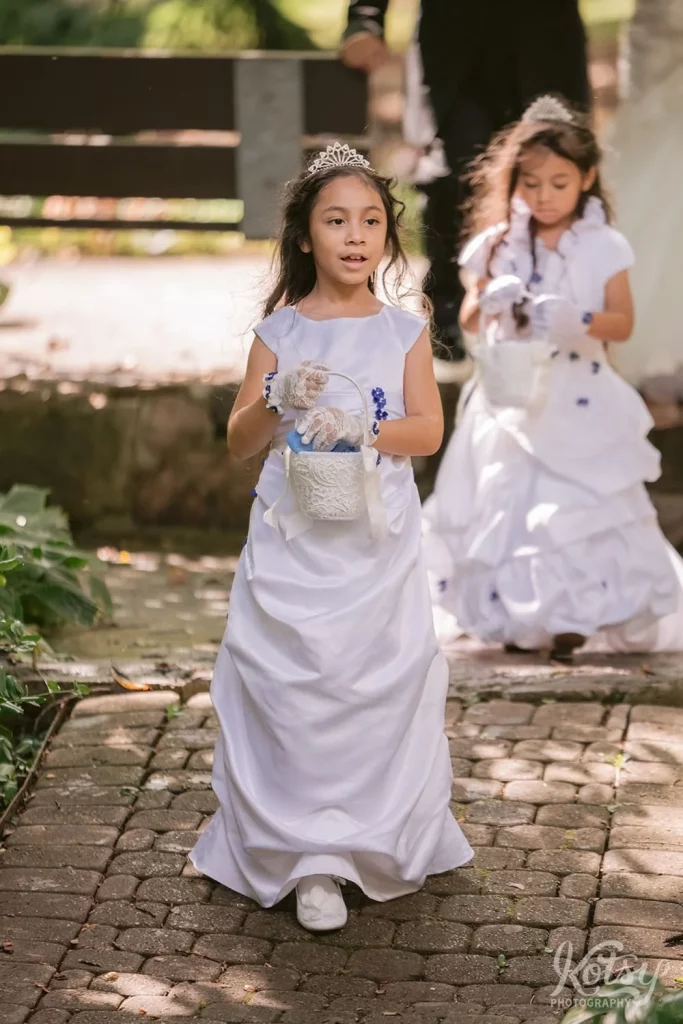 A flower girl in a white dress makes her way down the aisle at an outdoor wedding