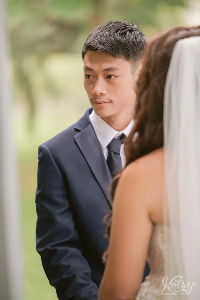 A groom looks off camera while holding his bride's hands at the alter