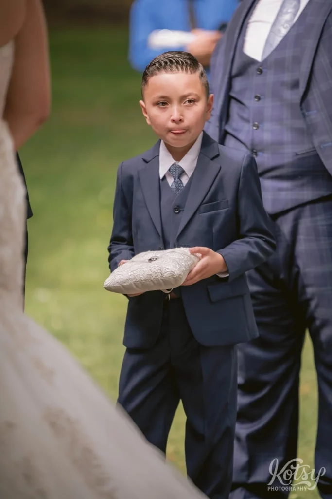 A candid shot of a ring bearer in a blue suit during an outdoor wedding ceremony
