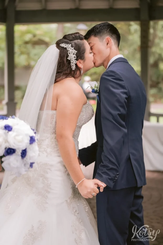 A bride and groom enjoy their first kiss during their outdoor wedding ceremony at Rosetta McClain Gardens in Toronto