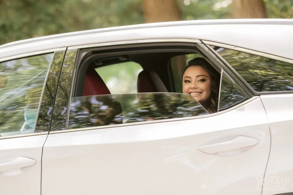 A bride smiles for the camera while sitting in a car upon arrival to her wedding ceremony
