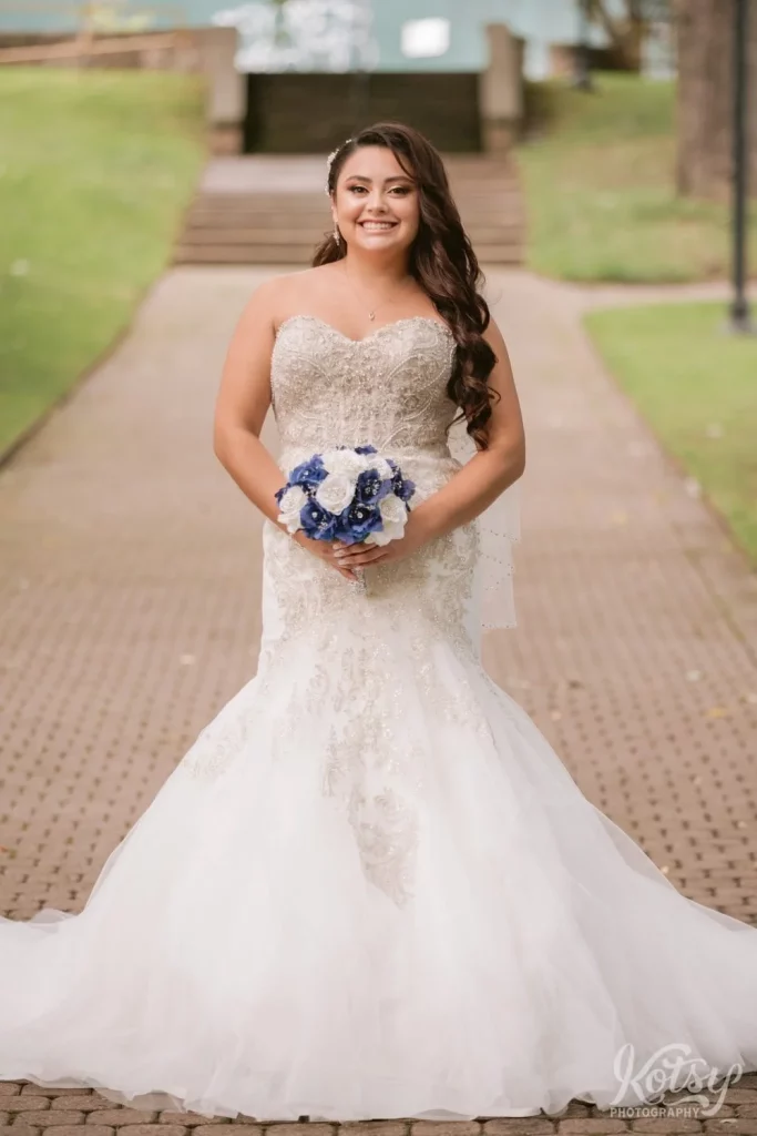 A bride poses for the camera in her wedding gown and blue and white flower bouquet
