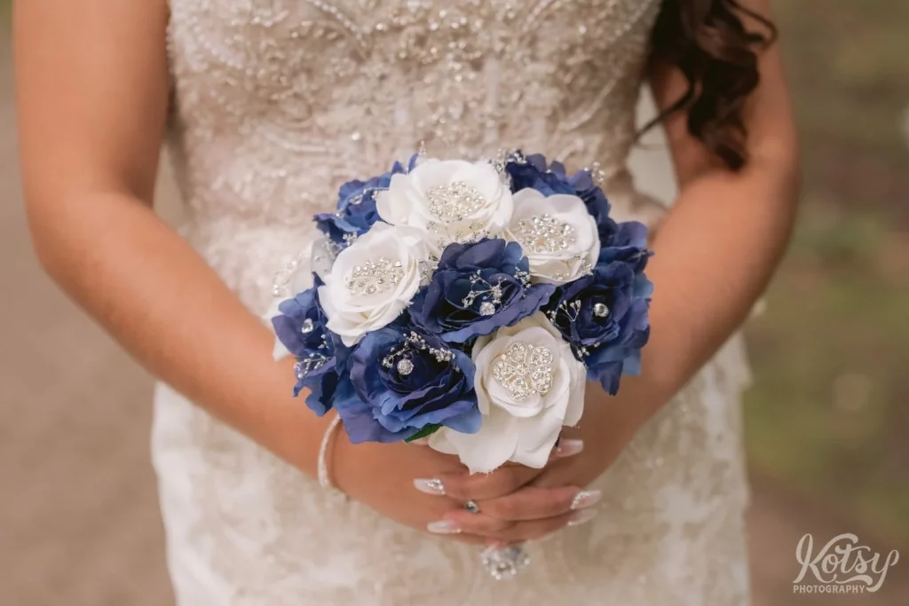 A close up shot of a blue and white rose bouquet held by a bride in white wedding gown