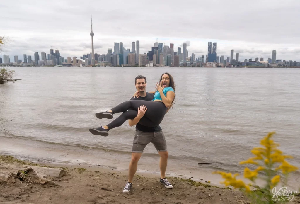 A man holds his new fiancé who shows off her engagement ring after their proposal on Toronto Islands