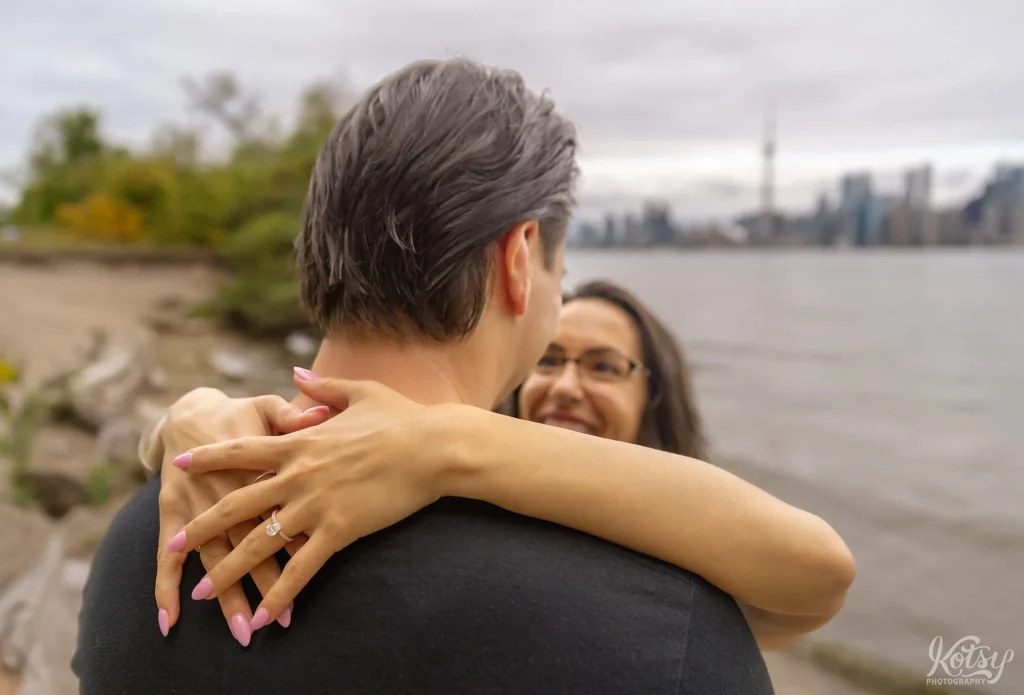A close up shot of an engagement ring on a woman's hand around a man's neck on Toronto Islands