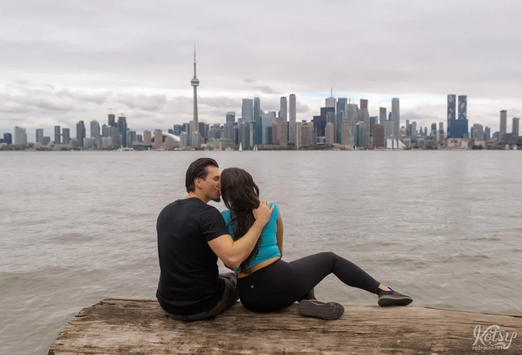 A couple kiss while sitting on a big log at Toronto Islands
