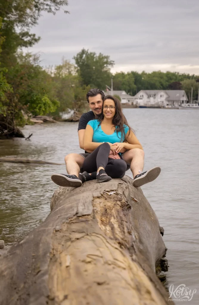 A couple smile for the camera while sitting on a big log on Toronto Islands