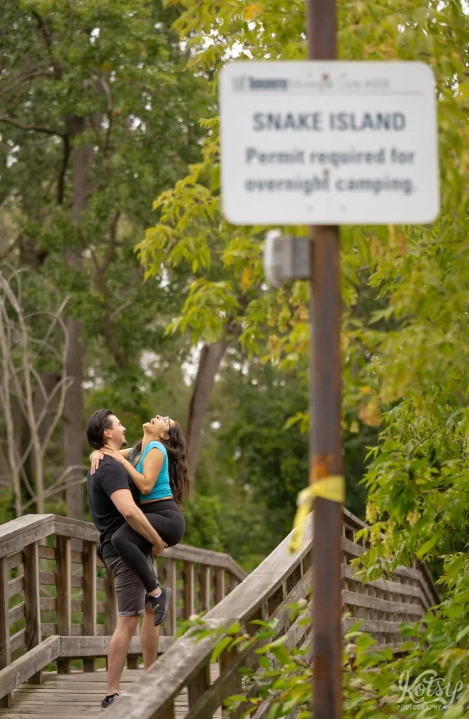 A woman reacts with glee as her fiancé holds her up on a wooden bridge on Snake Island in Toronto