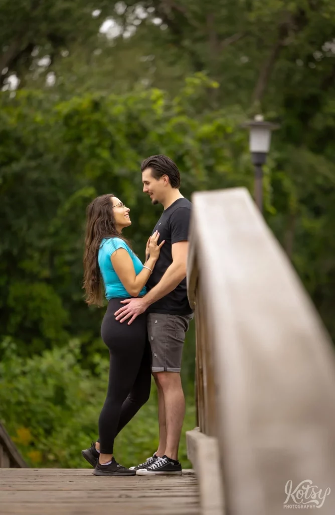 A couple look into each other's eyes while standing on a wooden bridge in Toronto