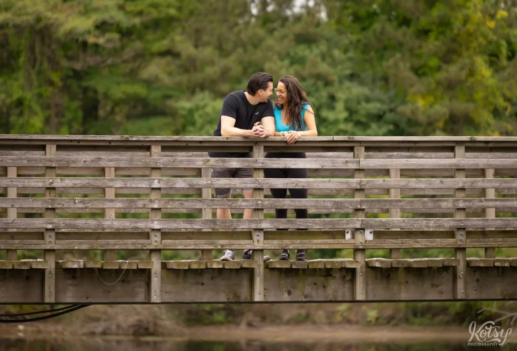 A couple smile each other while leaning on the guardrail of a wooden bridge on Snake Island
