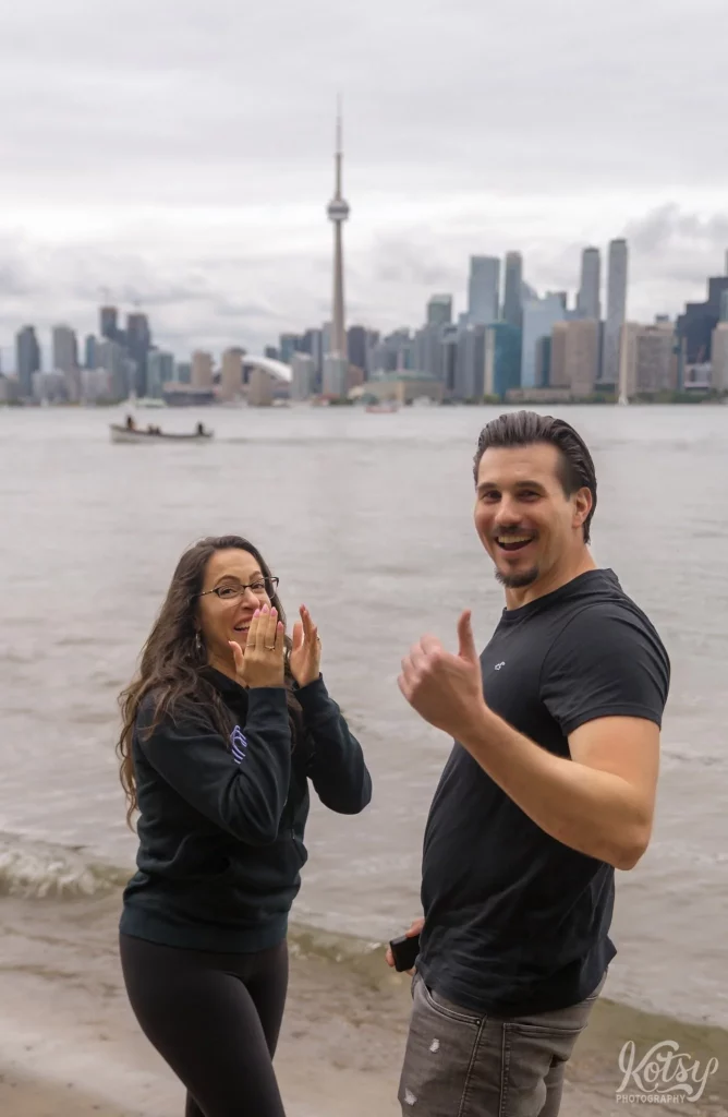 A couple reacts to a photographer's presence after getting engaged on a beach at Toronto Islands