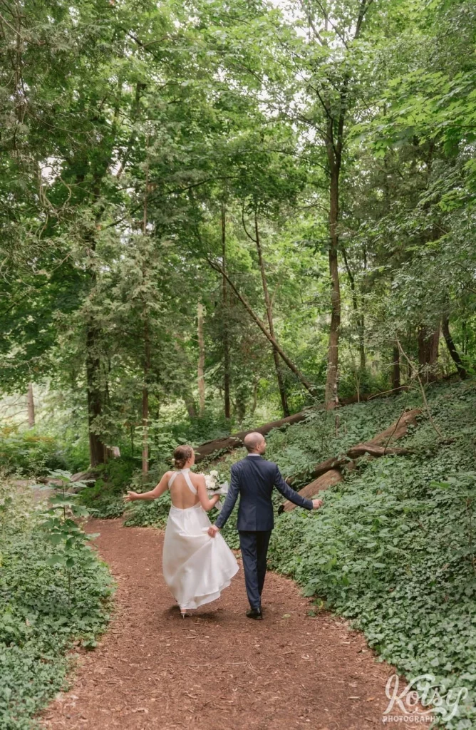 A bride and groom walk through a vast forest tall above them at Edwards Gardens in Toronto
