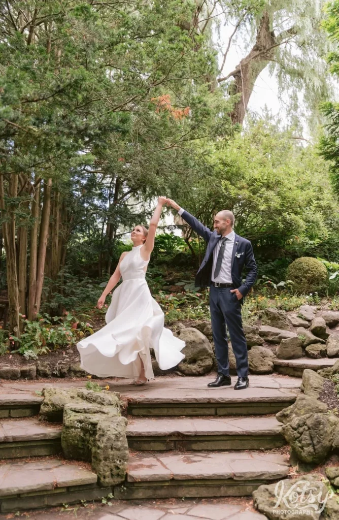 A groom spins his bride on a stone surface at Edwards Gardens in Toronto