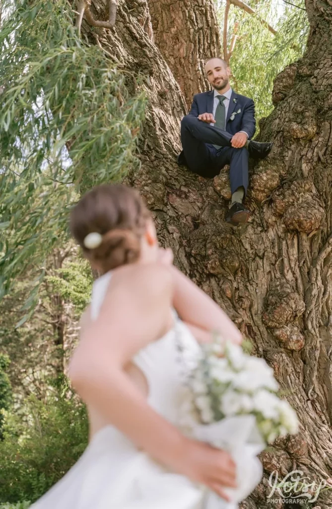 A bride blows a kiss to her groom sitting high up in a tree at Edwards Gardens in Toronto