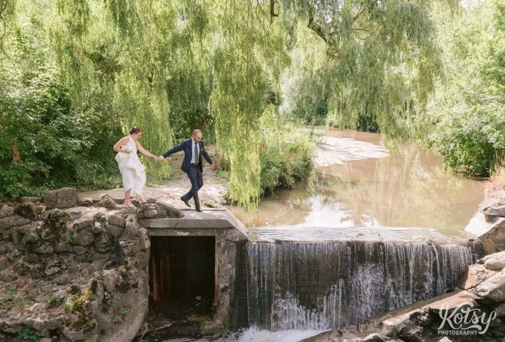 A groom leads his bride along a path to a waterfall at Edwards Gardens in Toronto