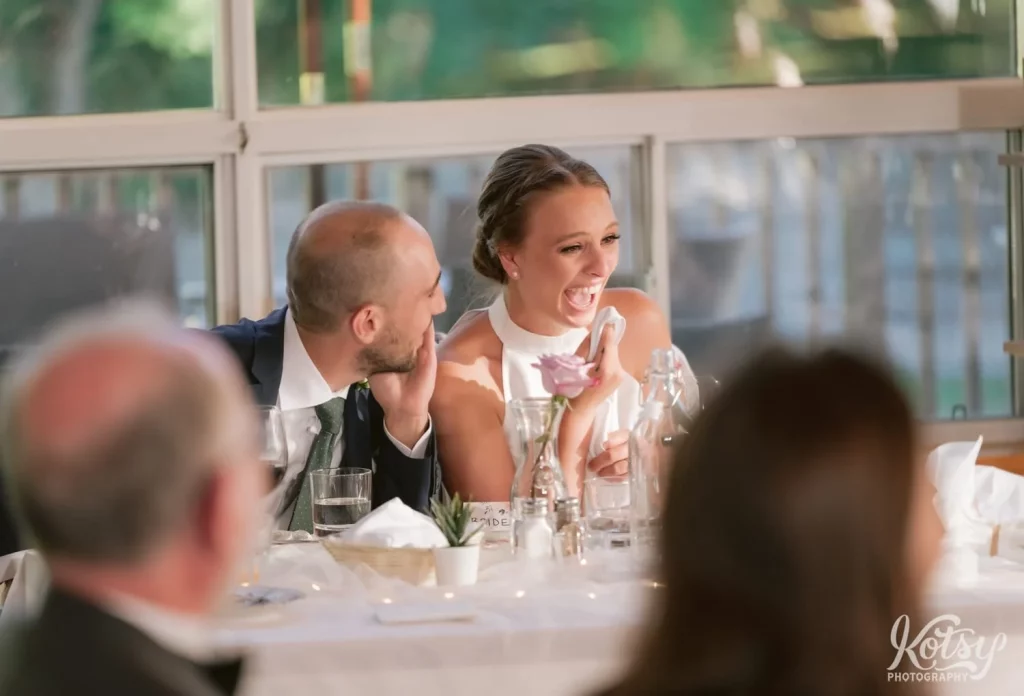 A bride and groom enjoy a laugh while sitting at their dinner table