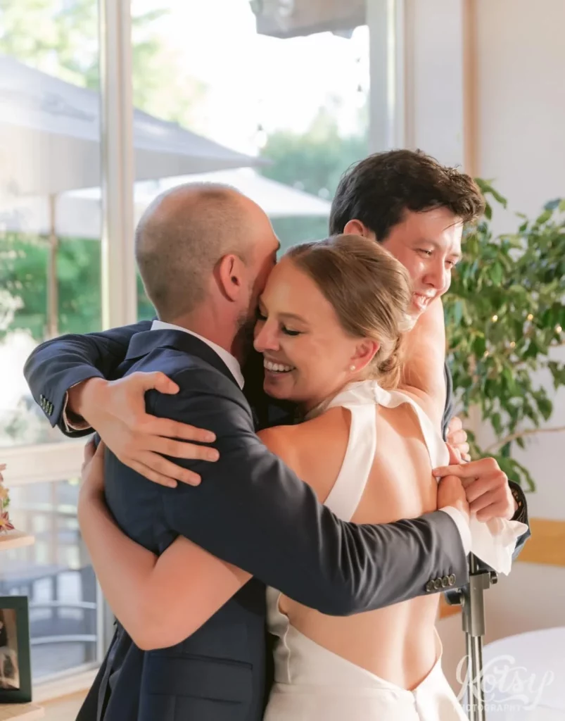 A bride and groom hug a friend after his speech during their wedding reception at The Prague