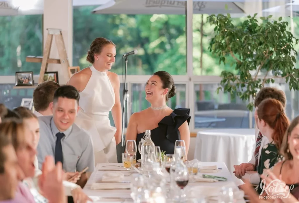 A bride and her friend enjoy a laugh at the end of a long table of guests at The Prague Restaurant