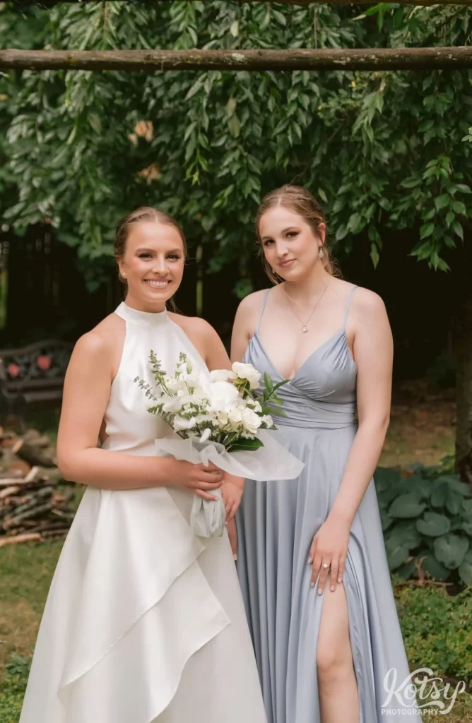 A bride poses for a photo with her sister in a backyard