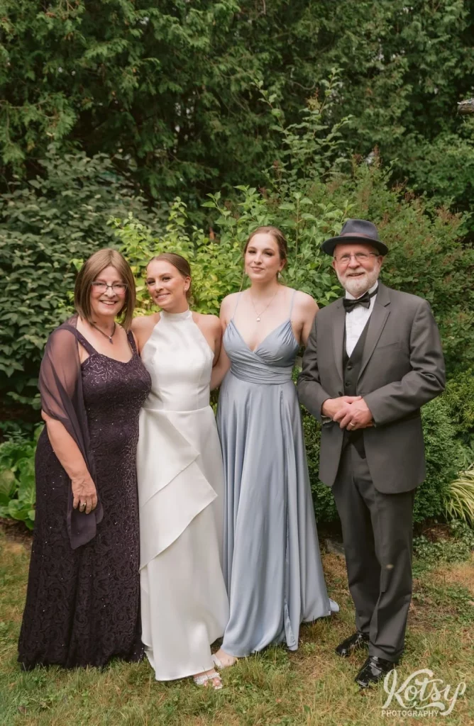 A bride poses for a family photo with her sister, mother and father