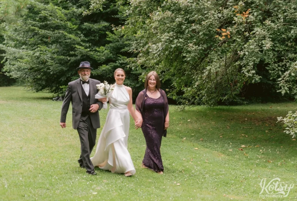 A bride walks with her parents through Edwards Gardens towards her wedding ceremony